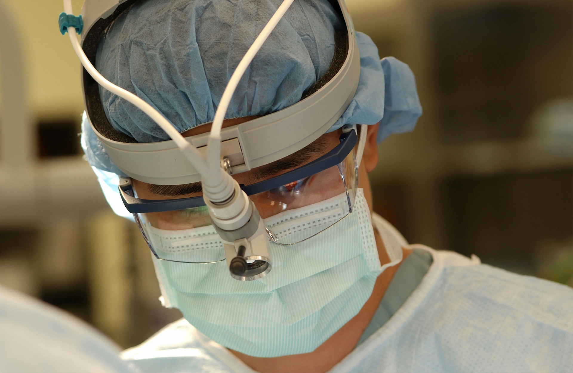Close-up of a surgeon wearing surgical gear and magnifying glasses focused during an operation.
