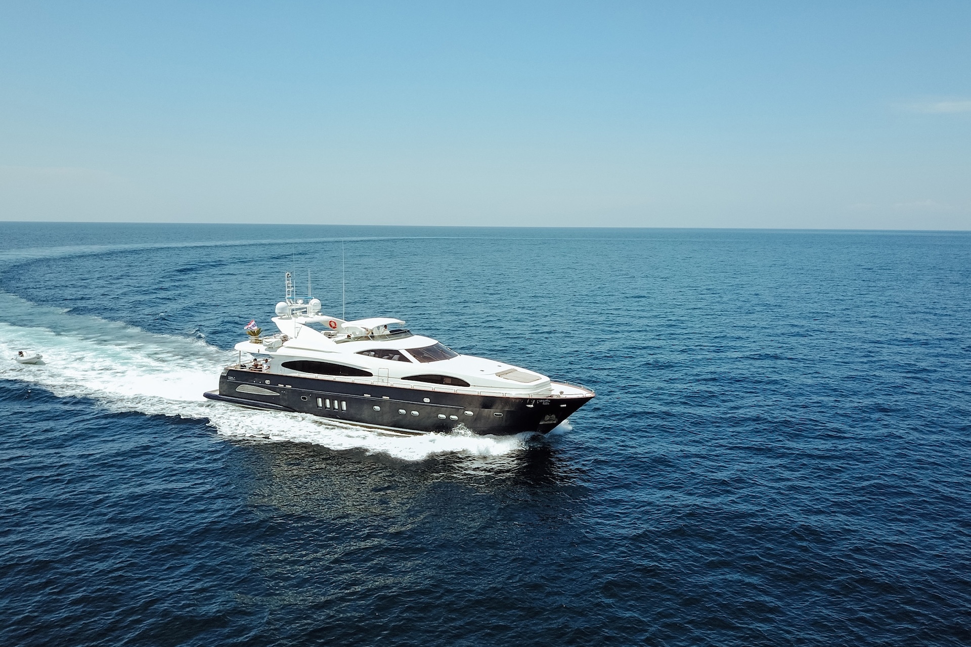 Luxury white yacht cruising through open blue ocean under a clear sky.