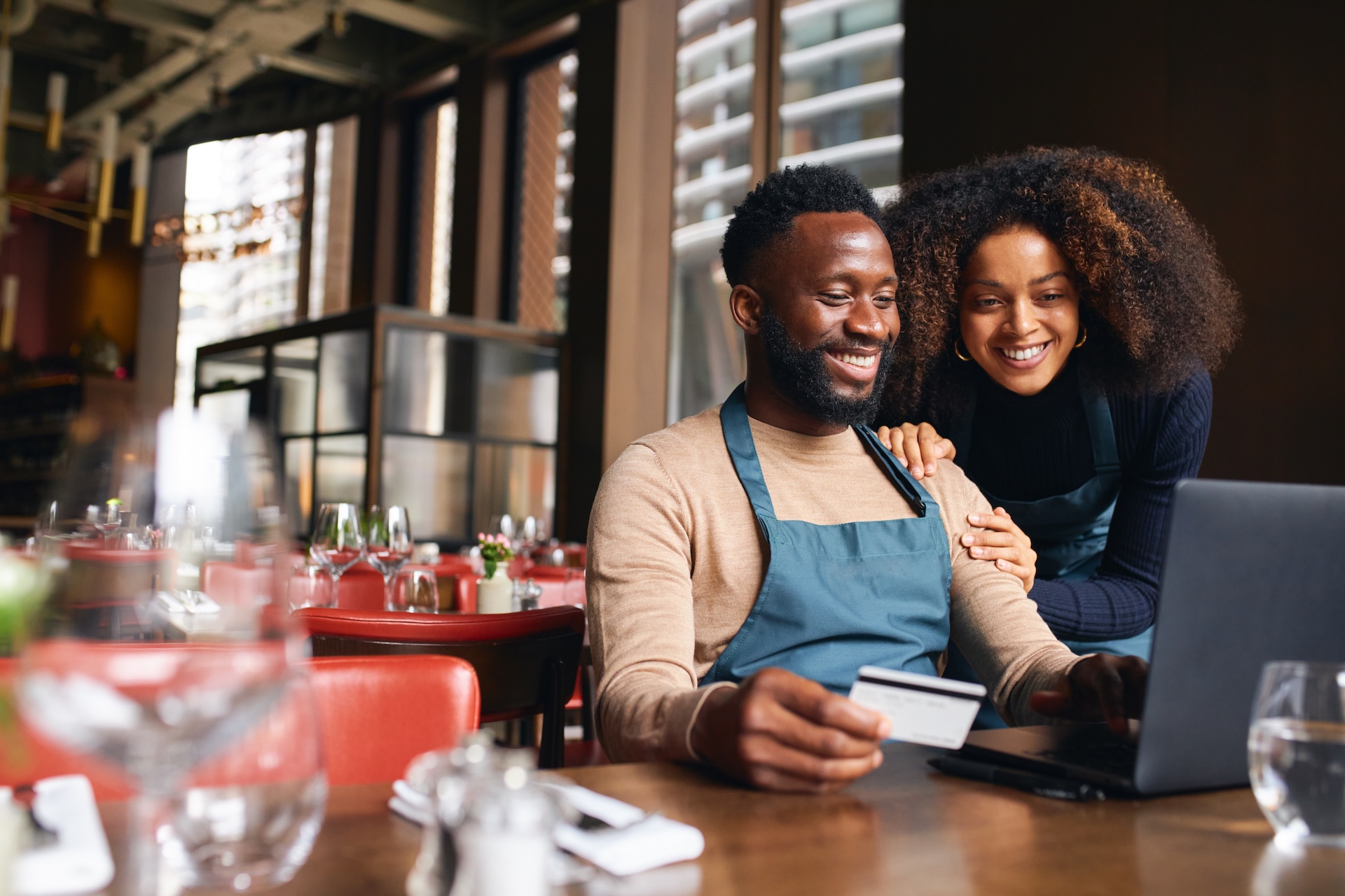 Two smiling people looking at a laptop screen, one has a credit card in his hand