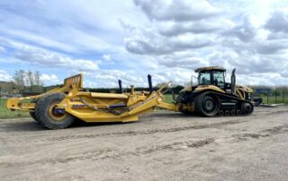 Large yellow Caterpillar tracked tractor pulling a heavy-duty land scraper on a construction site.