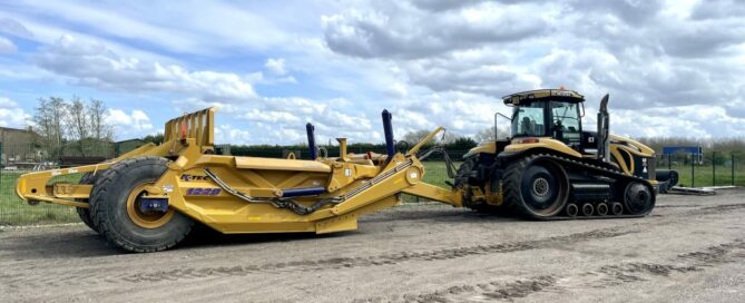 Large yellow Caterpillar tracked tractor pulling a heavy-duty land scraper on a construction site.