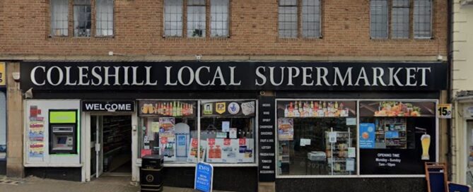 Front view of Coleshill Local Supermarket with various signs in the windows and a visible 'Welcome' sign above the entrance.