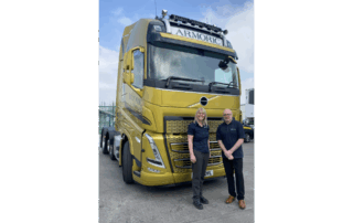 Full version of gold Volvo truck labeled 'ARMORIC' with two people smiling in front.