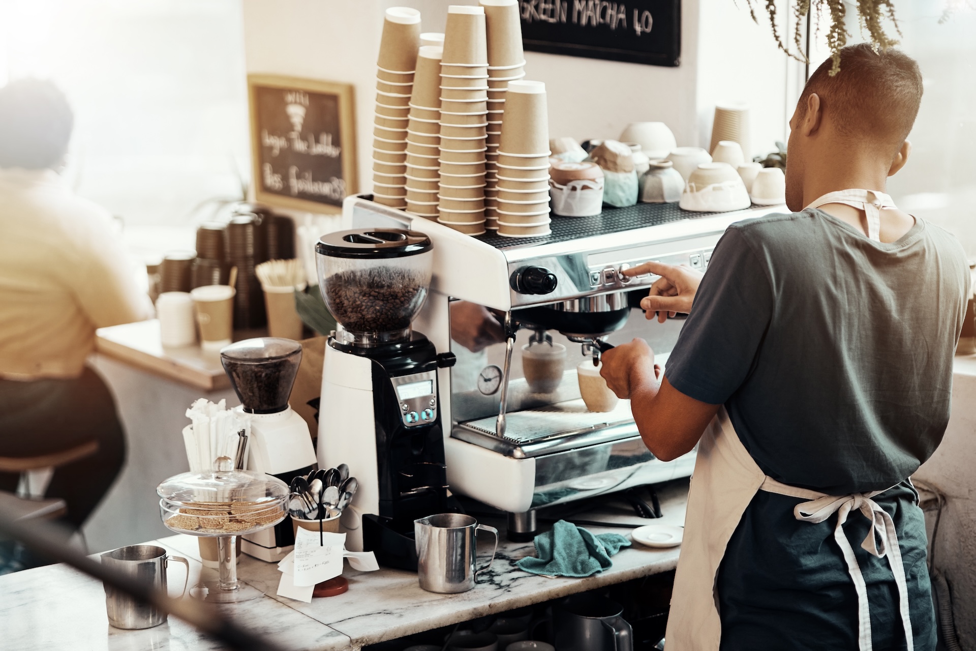 Cafe,Barista,,Man,And,Server,At,Coffee,Machine,To,Prepare Barista operating a commercial espresso machine in a cozy coffee shop.
