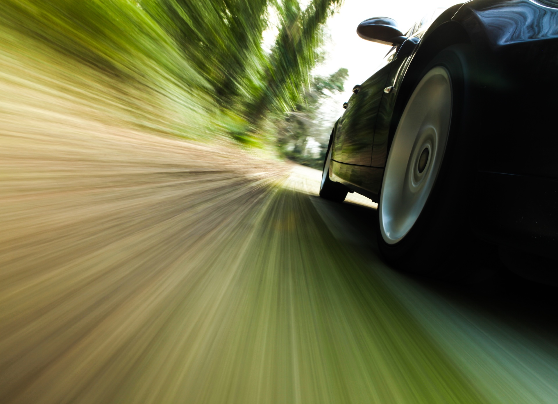 Front,Side,View,Of,Black,Car,Driving,Fast. A side view of a black car speeding down a country road