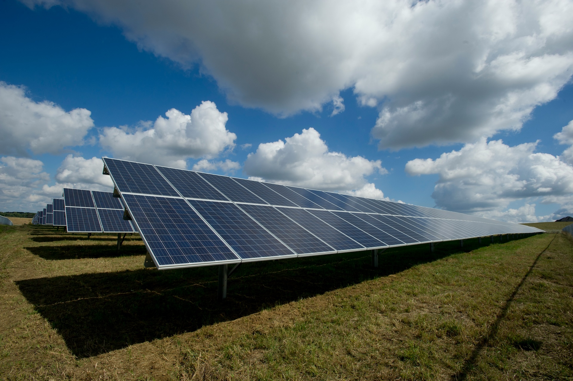 american-public-power-association-513dBrMJ_5w-unsplash A row of solar panel in a field on a sunny day with some cloud coverage