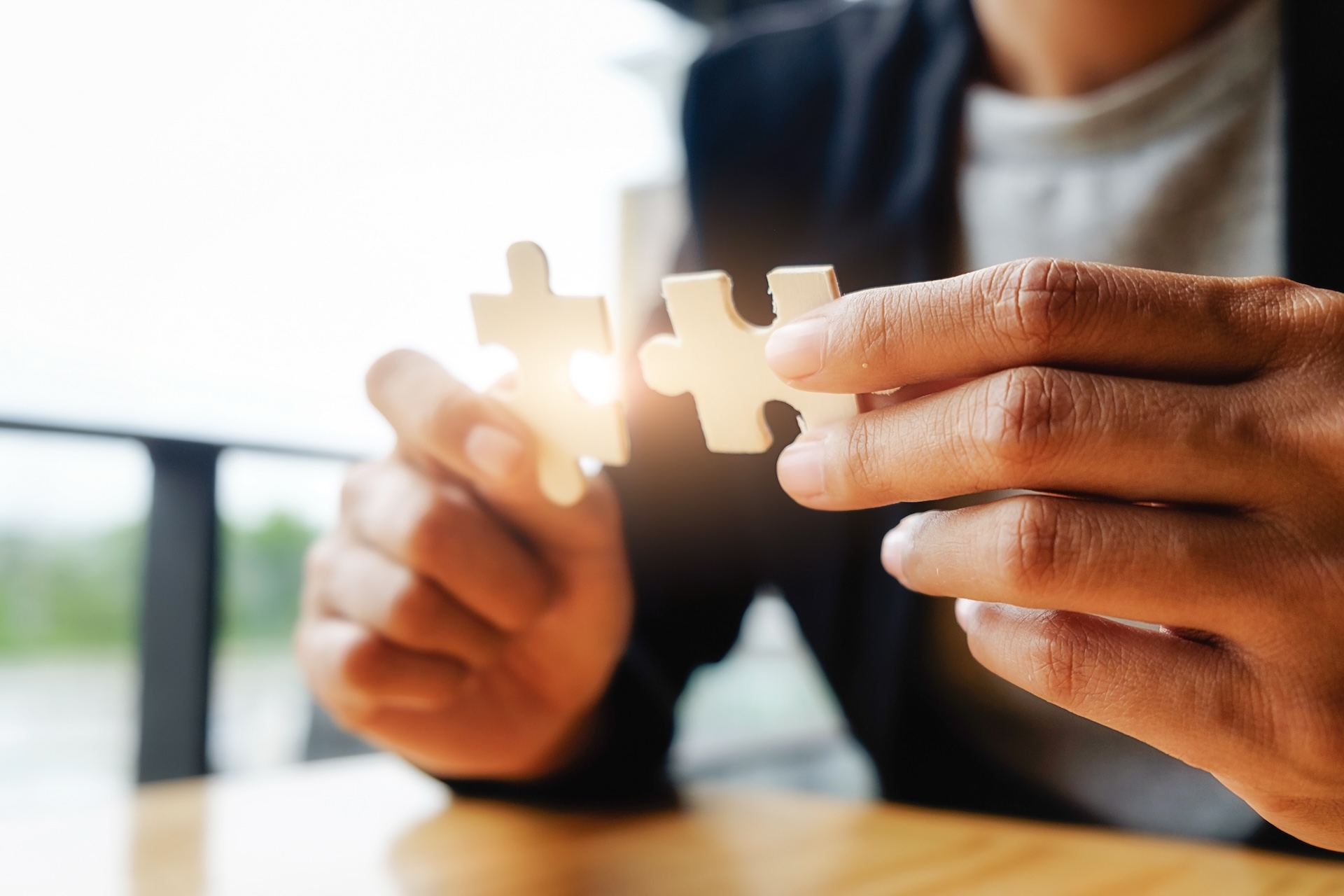 the hands of a business woman connecting two white jigsaw pieces