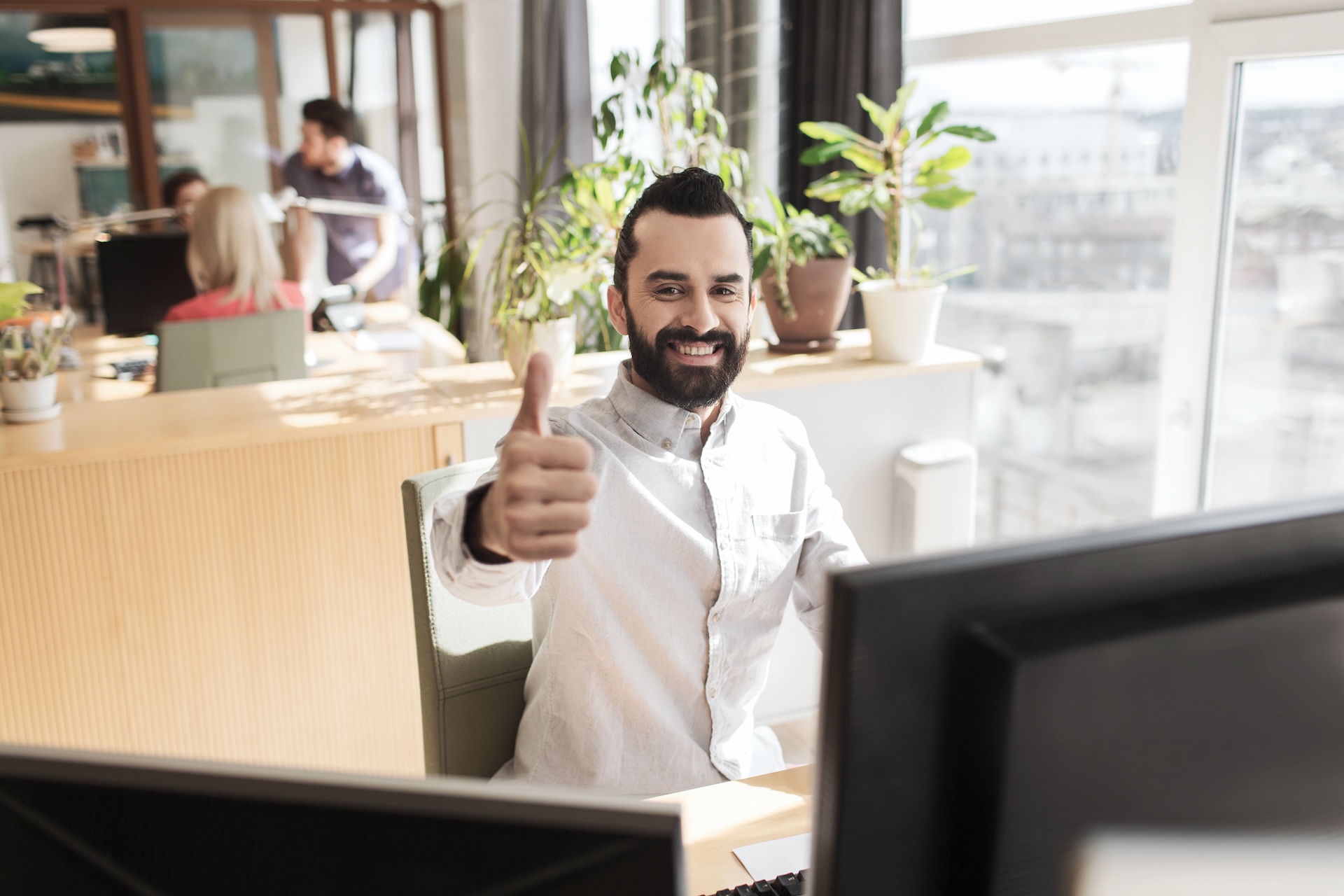 Smiling businessman in a casual office giving a thumbs-up, representing startup success or team values.