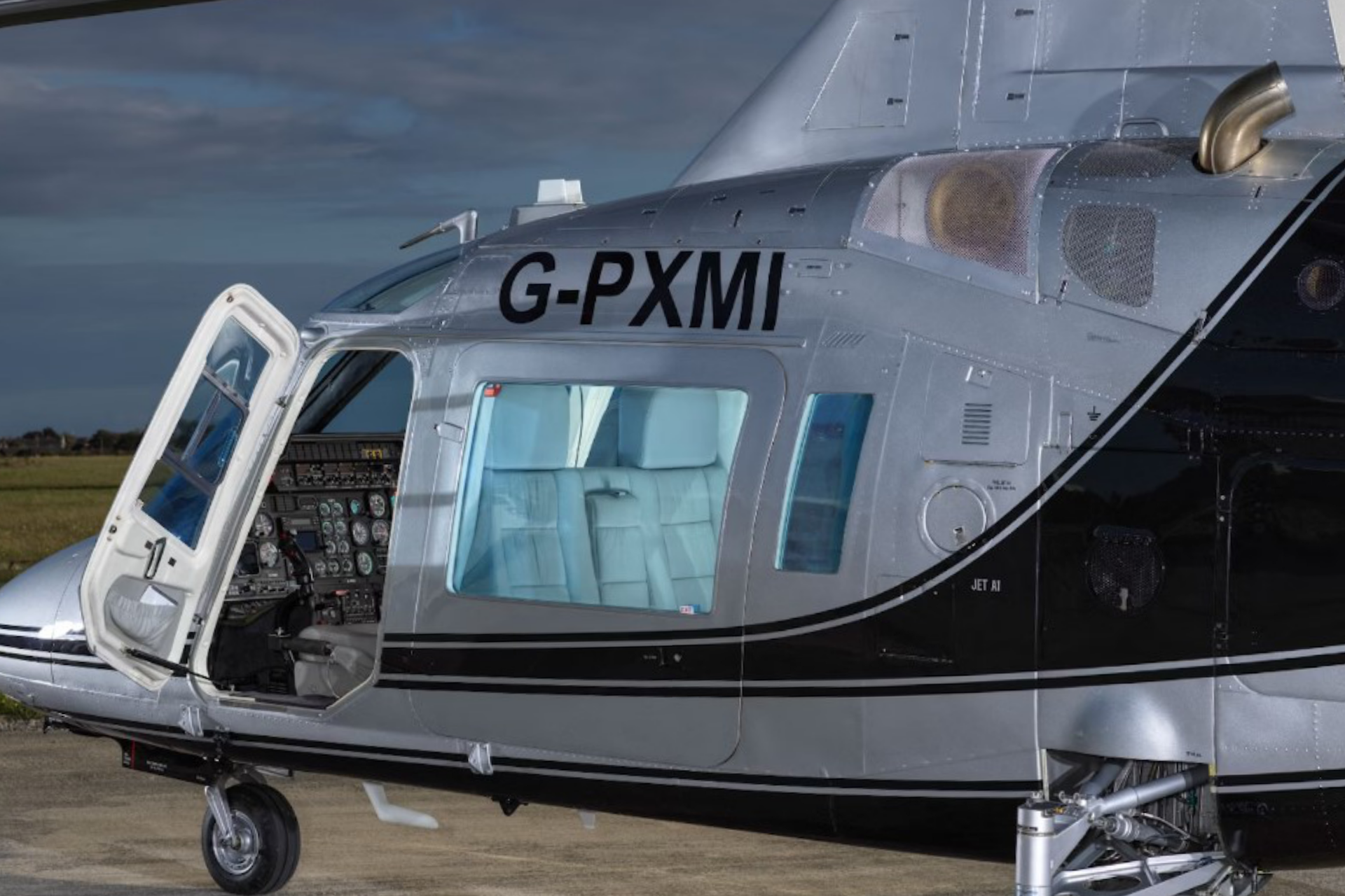 chopper1 Close-up side view of a silver and black helicopter with the door open, tail number G-PXMI visible, and the cockpit instruments exposed.
