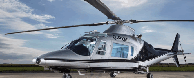 High-resolution image of a silver and black helicopter marked G-PXMI, sitting on an airstrip with the sun shining overhead.