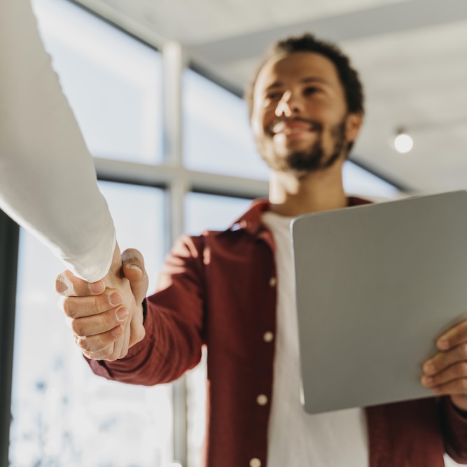 Two professionals shaking hands across a desk, indicating partnership, agreement, or client relations.
