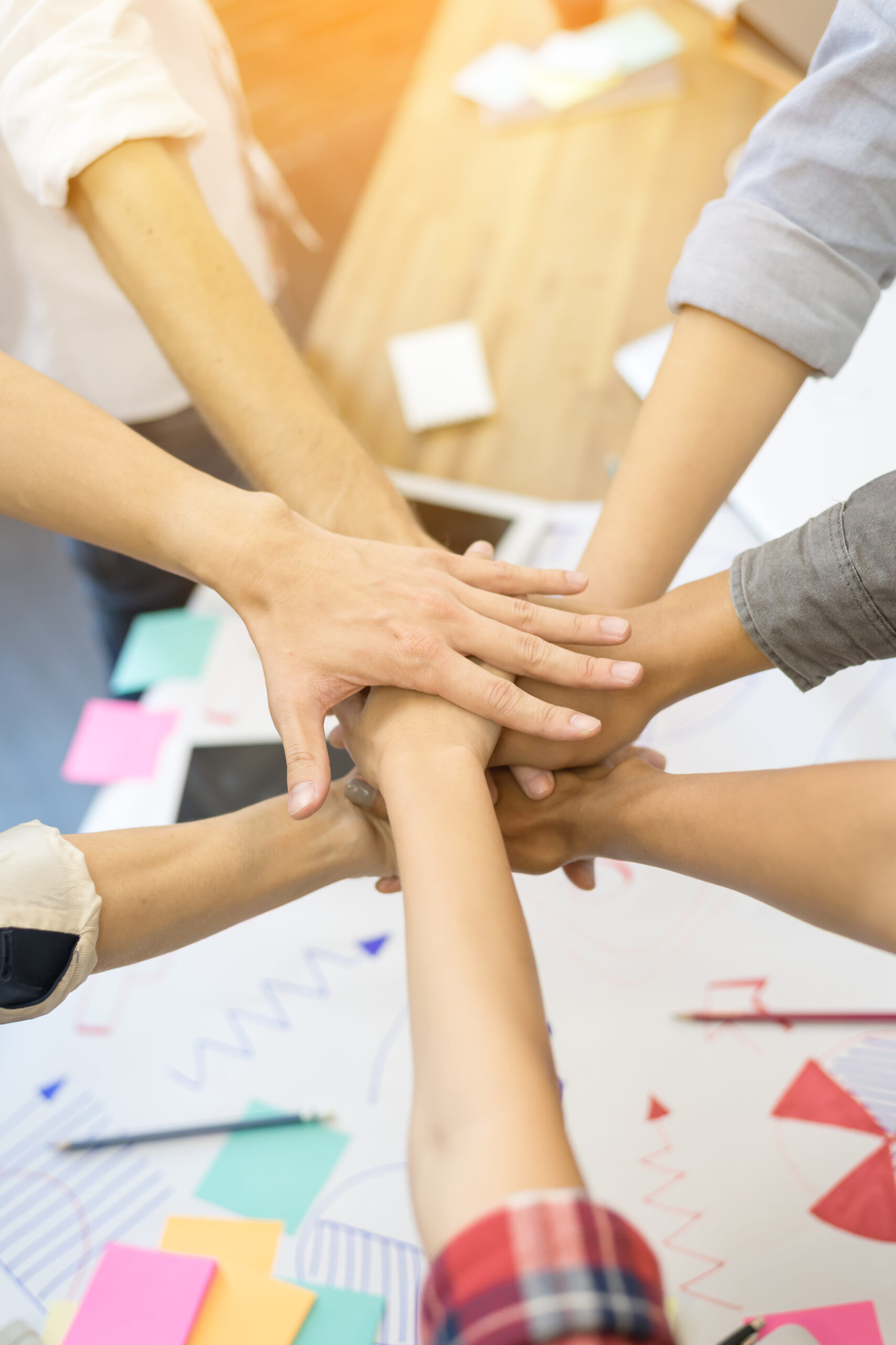 close-up-hand-s-asian-group-professional-colleagues-join-hands-together-our-purpose Group of professionals placing hands together in a gesture of unity, symbolizing teamwork and purpose.
