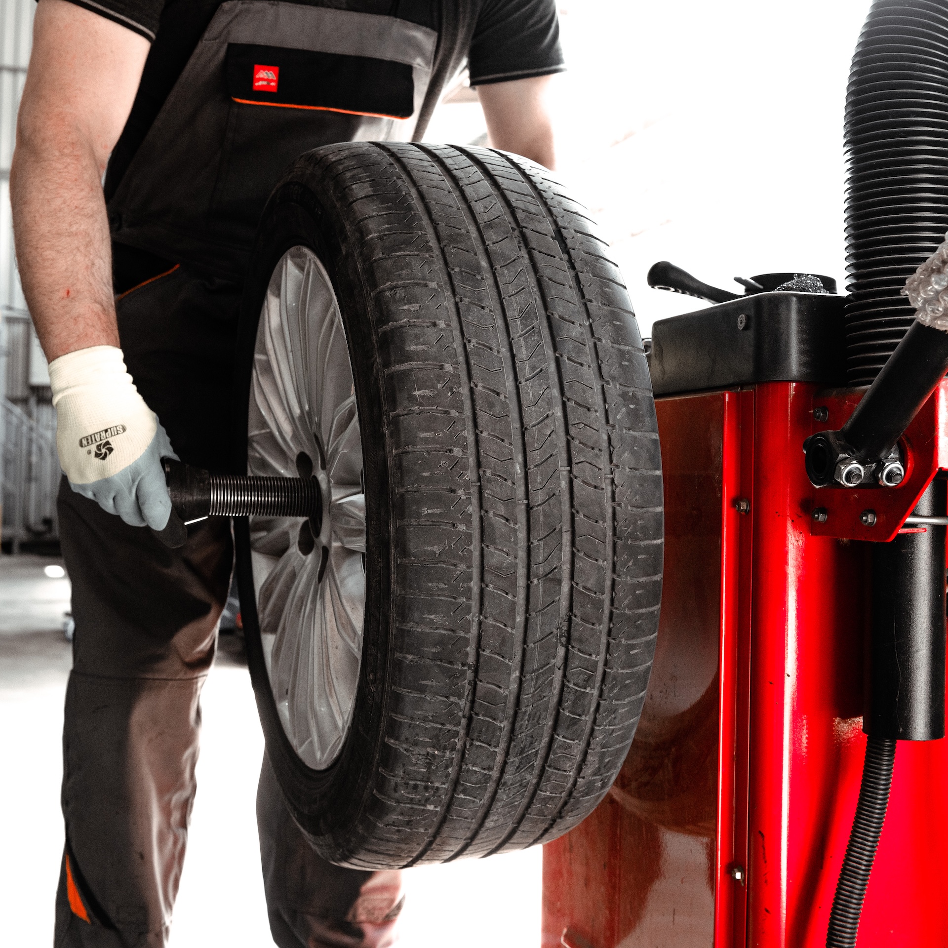garage_finance-man-is-working-tire-that-is-red-black Man in a garage working on a large red and black tire, representing vehicle repair or finance.