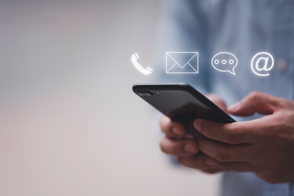 A business man holding a smart phone with symbols for call, email and chat showing above the phone