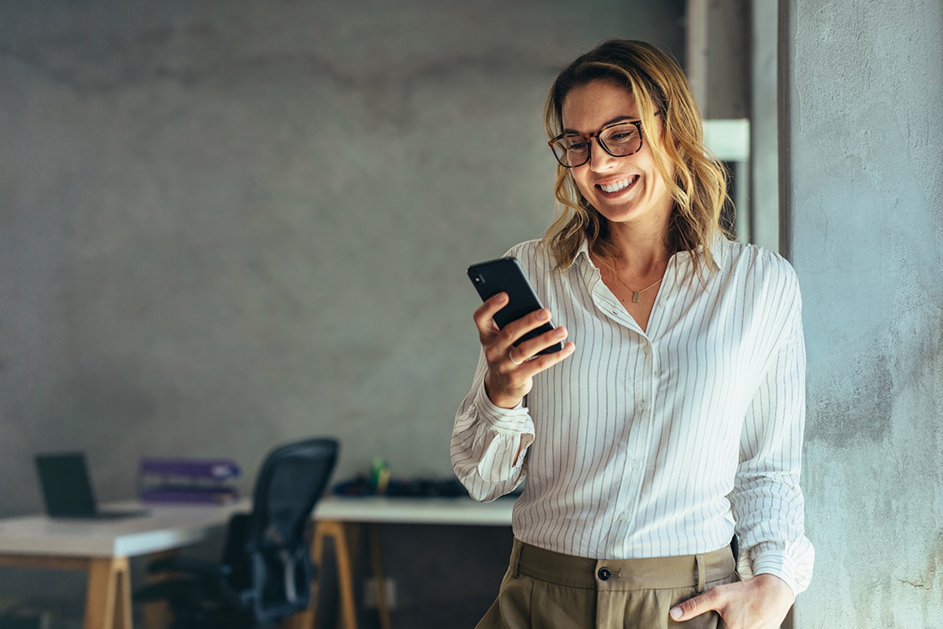 A smiling businesswoman in a white shirt using her phone in an office