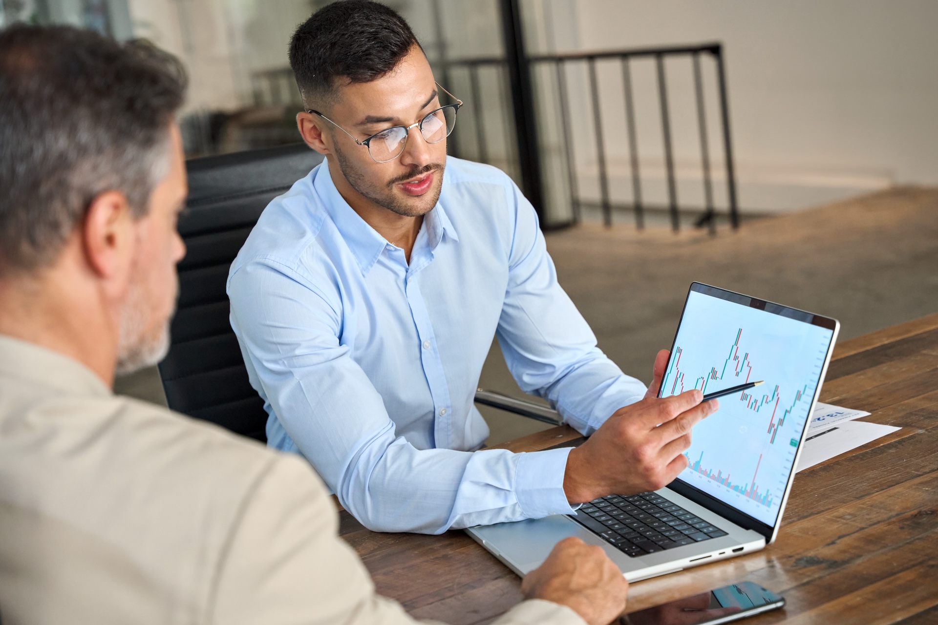 A image of two business men sitting at a table discussing a graph on a laptop