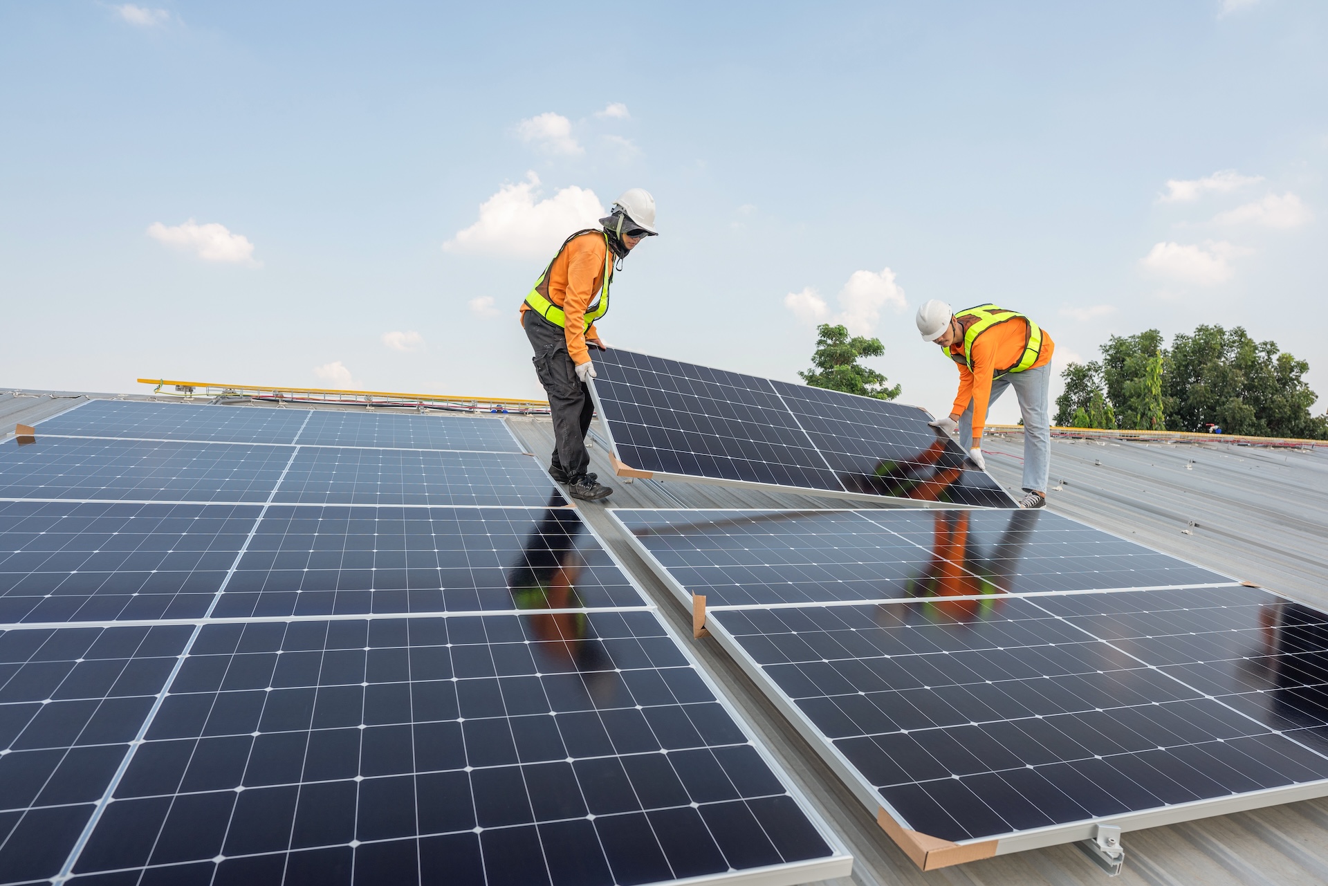 A image of two men in safety clothing installing solar panel on a factory roof