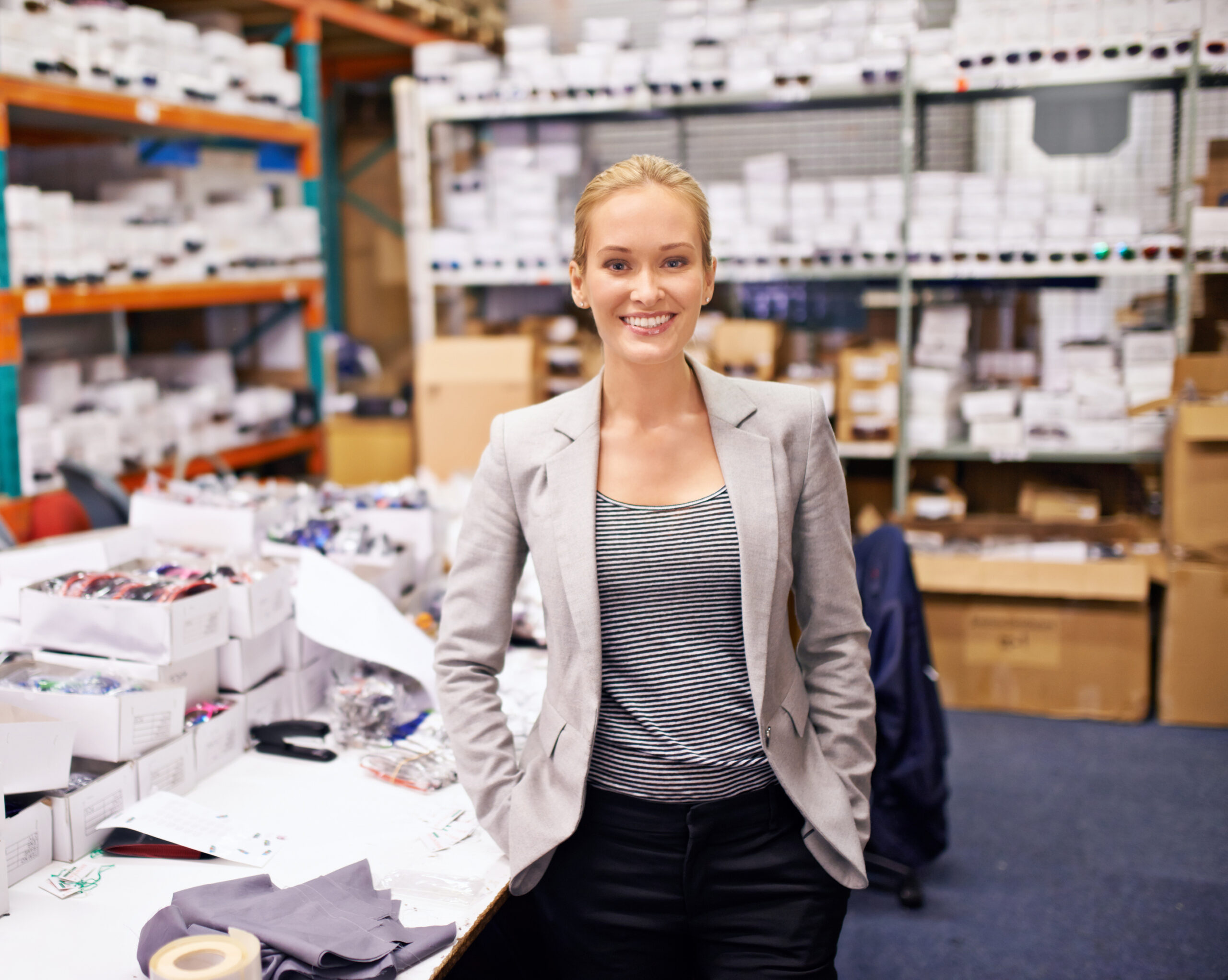 Woman standing in a warehouse aisle among stocked shelves, representing logistics or stock management.
