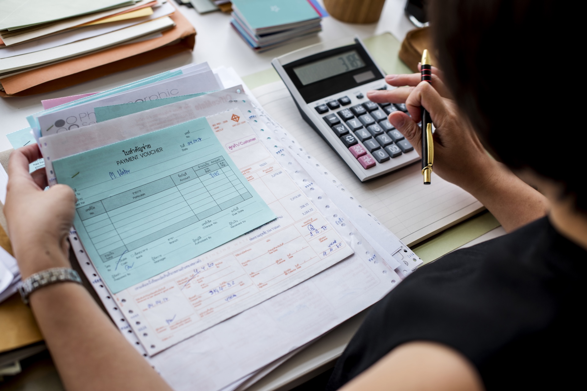 Woman seated at a desk surrounded by documents, deeply focused on financial or administrative paperwork.